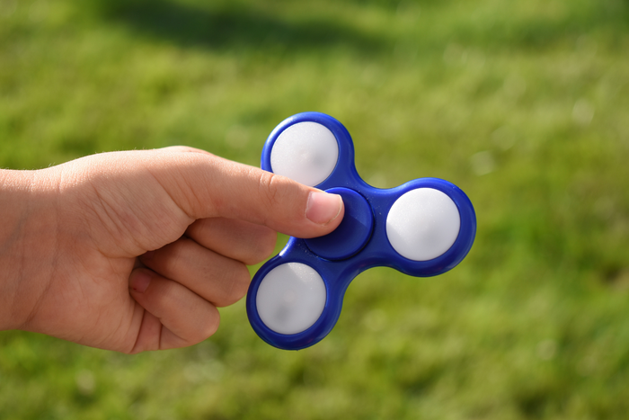 Hand holding a blue and white three-pronged fidget spinner outdoors with a green grass background.
