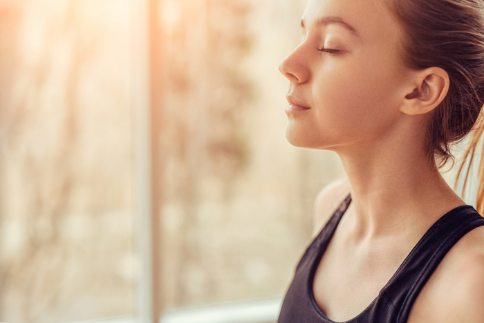 Girl with closed eyes practicing calming breathing techniques near window light