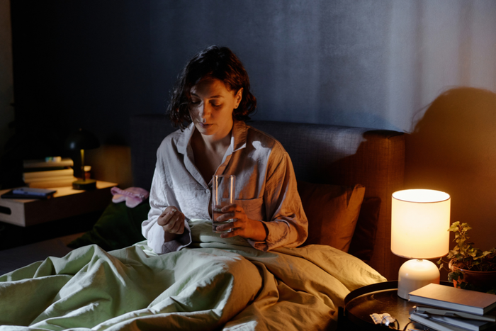 Woman sitting in bed at night holding a glass of water and supplement, preparing to take L-theanine for sleep support.