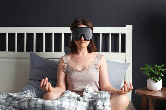 Woman wearing sleep mask practicing meditation for anxiety and sleep in bed