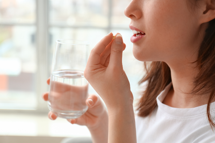 A person holds a glass of water and a pill, about to take medication.