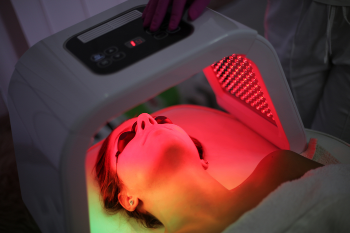 Woman receiving red light therapy on the face with LED panel device