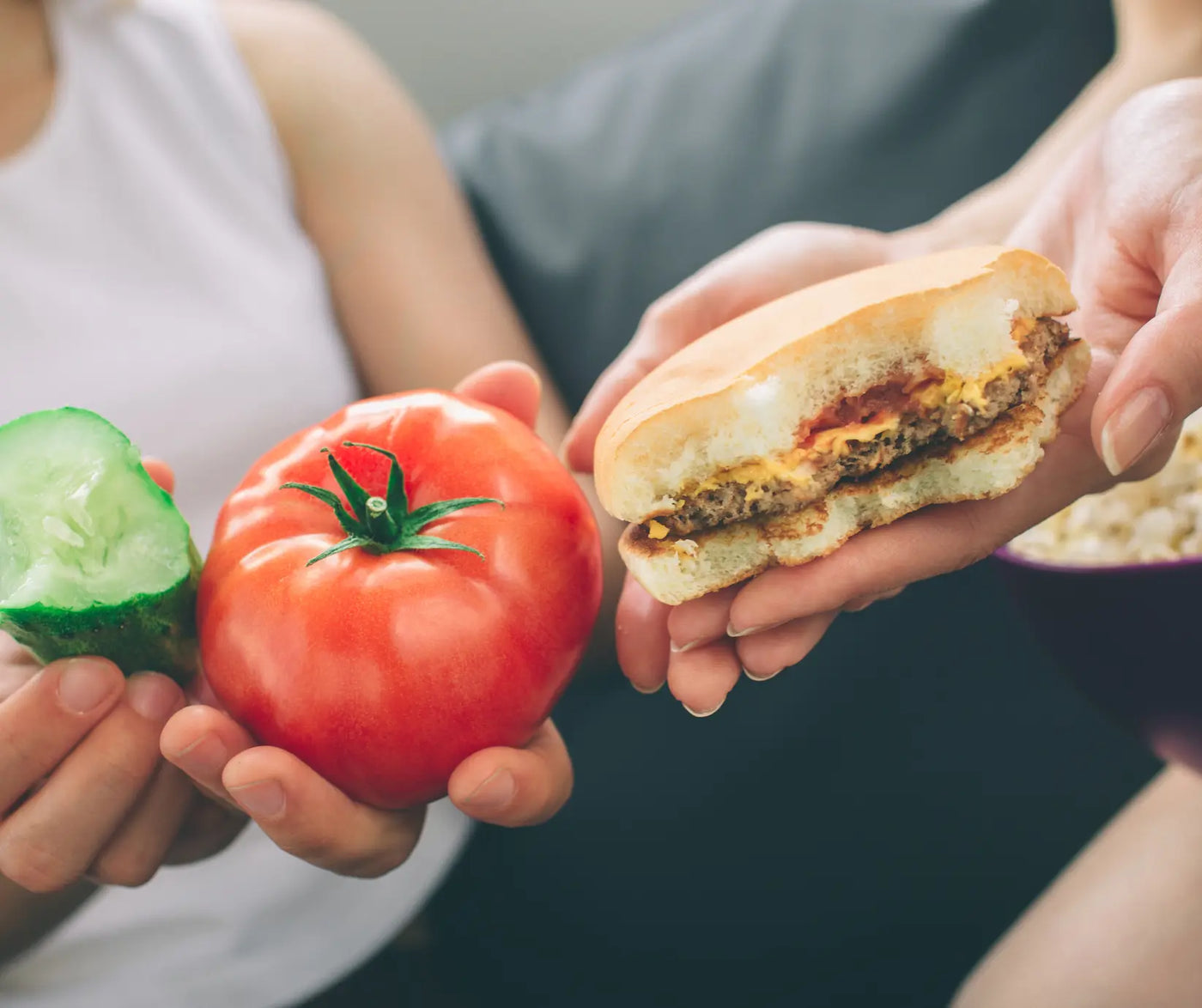 Two people with one holding a vegetables, while the other holding a hamburger.