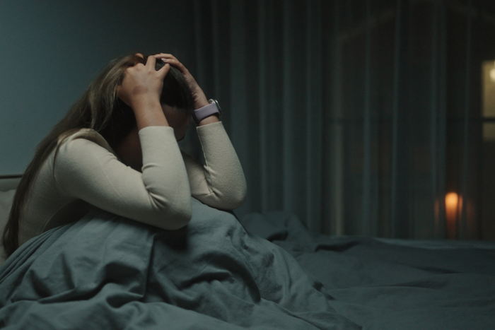 Woman sitting awake in bed with her hands on her head, representing nighttime anxiety and restlessness after melatonin use.