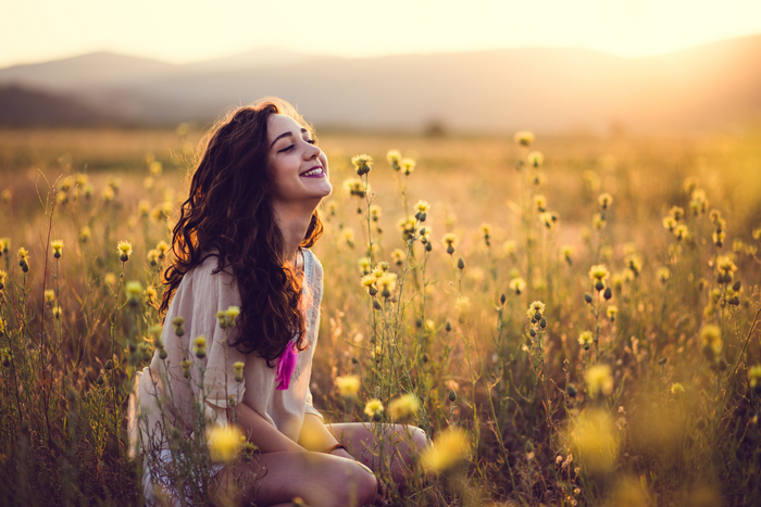 Woman smiling while sitting in a field of flowers.