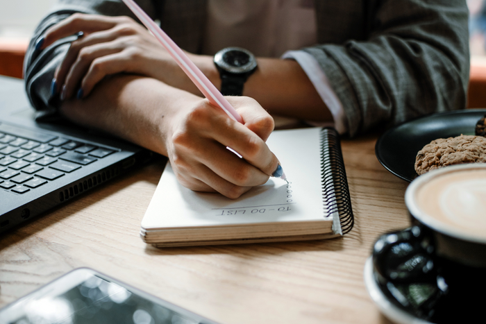 A close-up of a person’s hands writing in a planner.