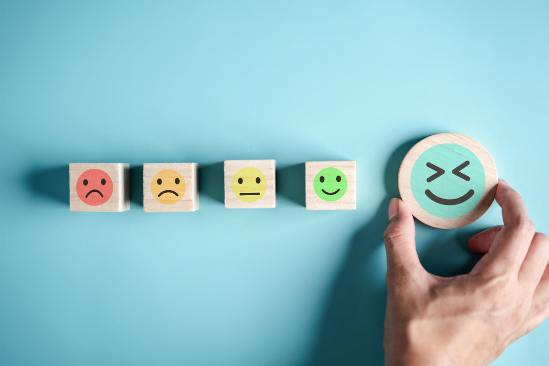 Hand selecting a happy face block from a row of emotional faces ranging from sad to happy, representing dopamine's role in mood improvement.