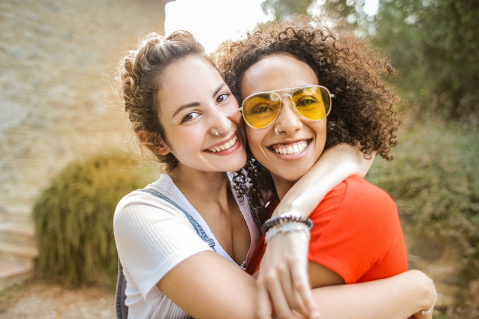 Two friends smiling at the camera and hugging each other.