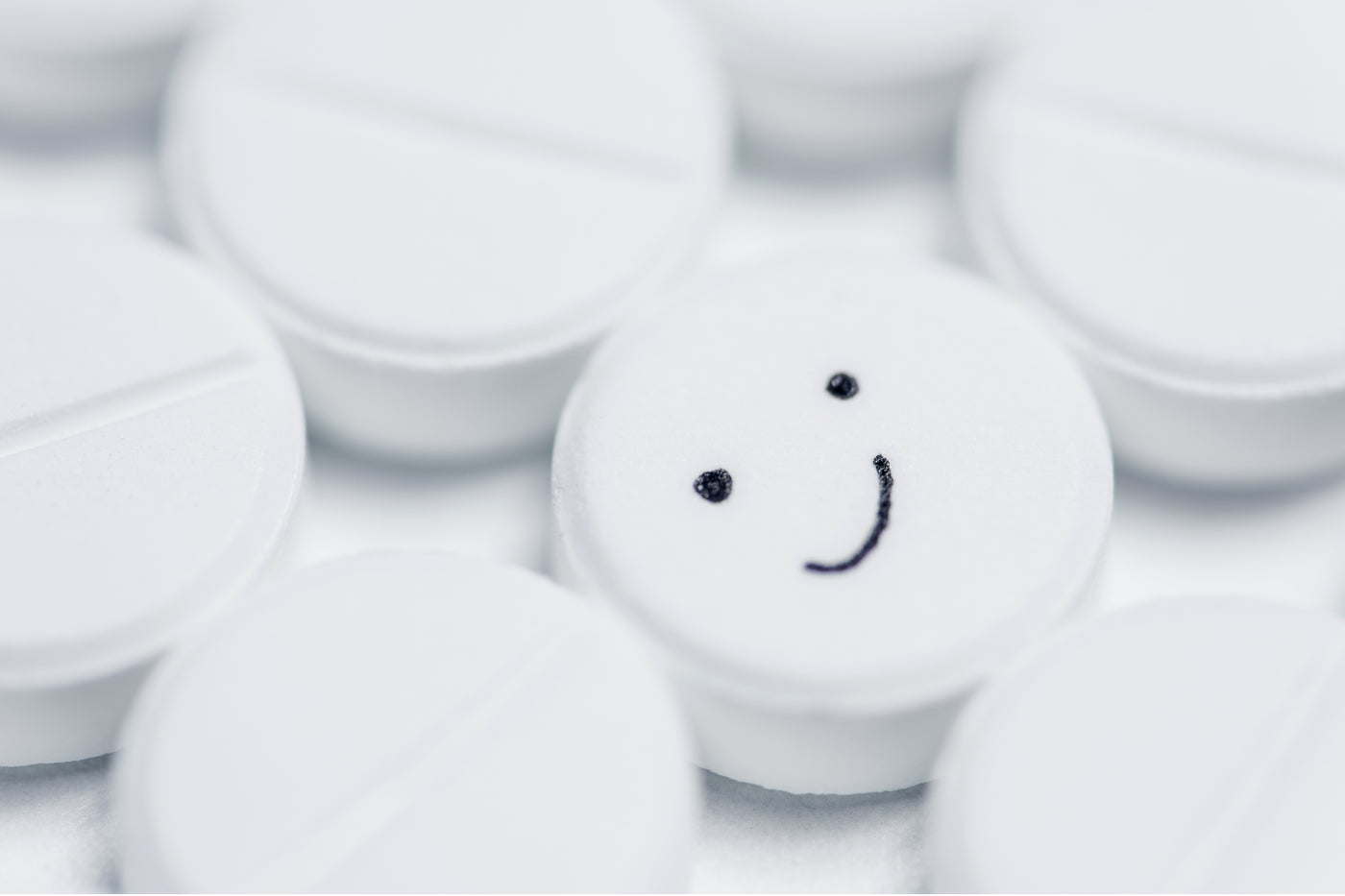 Close‑up of white tablets with one pill showing a smiley face, symbolizing the idea of a natural 'happy pill' without a prescription