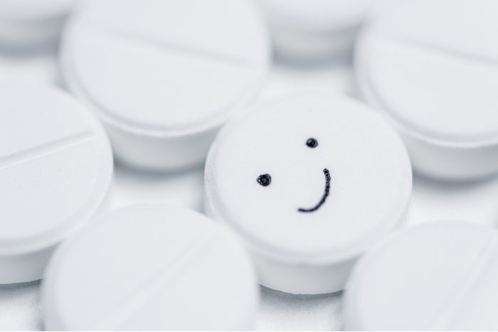 Close‑up of white tablets with one pill showing a smiley face, symbolizing the idea of a natural 'happy pill' without a prescription