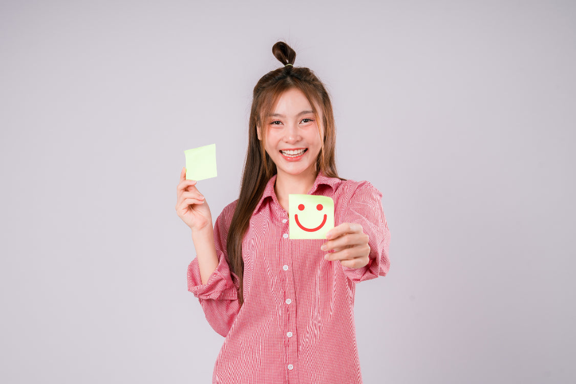 Smiling woman holding a happy face note symbolizing improved mood after addressing serotonin deficiency symptoms
