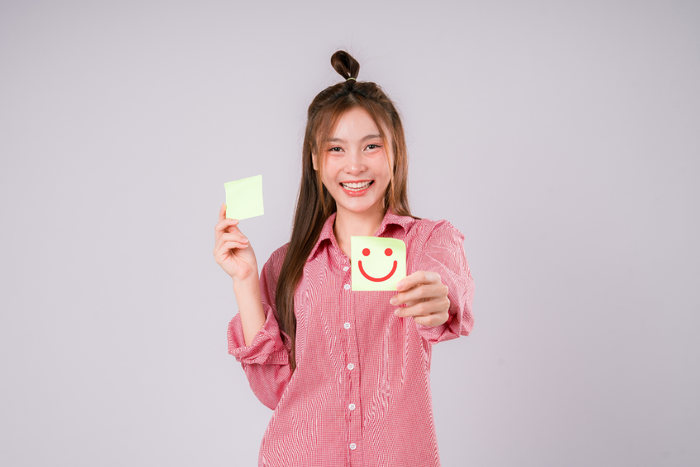 Smiling woman holding a happy face note symbolizing improved mood after addressing serotonin deficiency symptoms