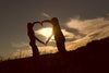 Two people making a heart with their arms in front of sunset
