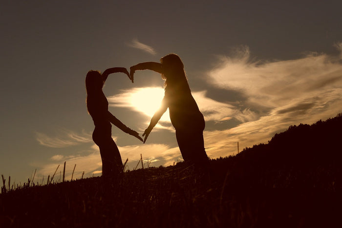 Two people making a heart with their arms in front of sunset
