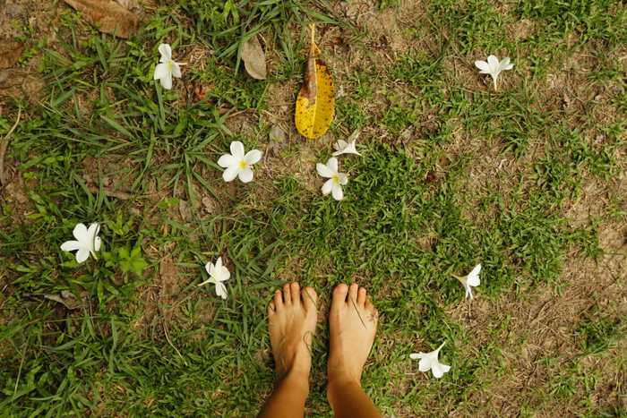 Feet touching on grass with flowers.