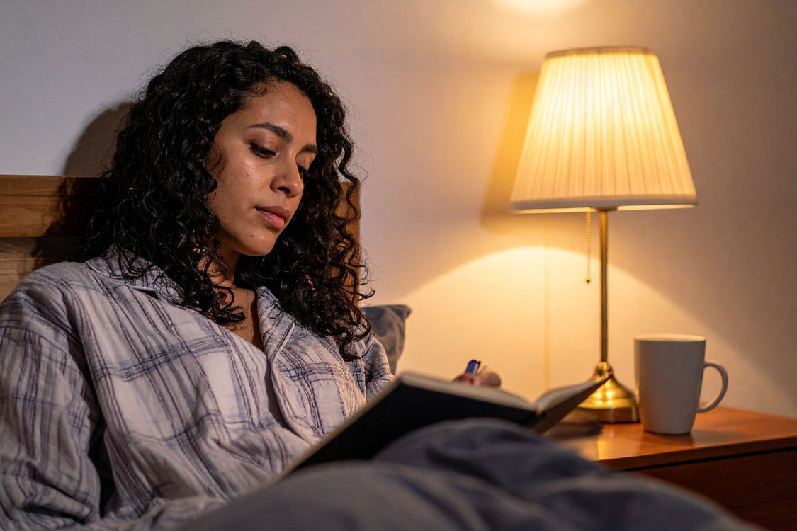 Woman journaling before bed under warm light, showing a calming nighttime writing routine for better sleep.