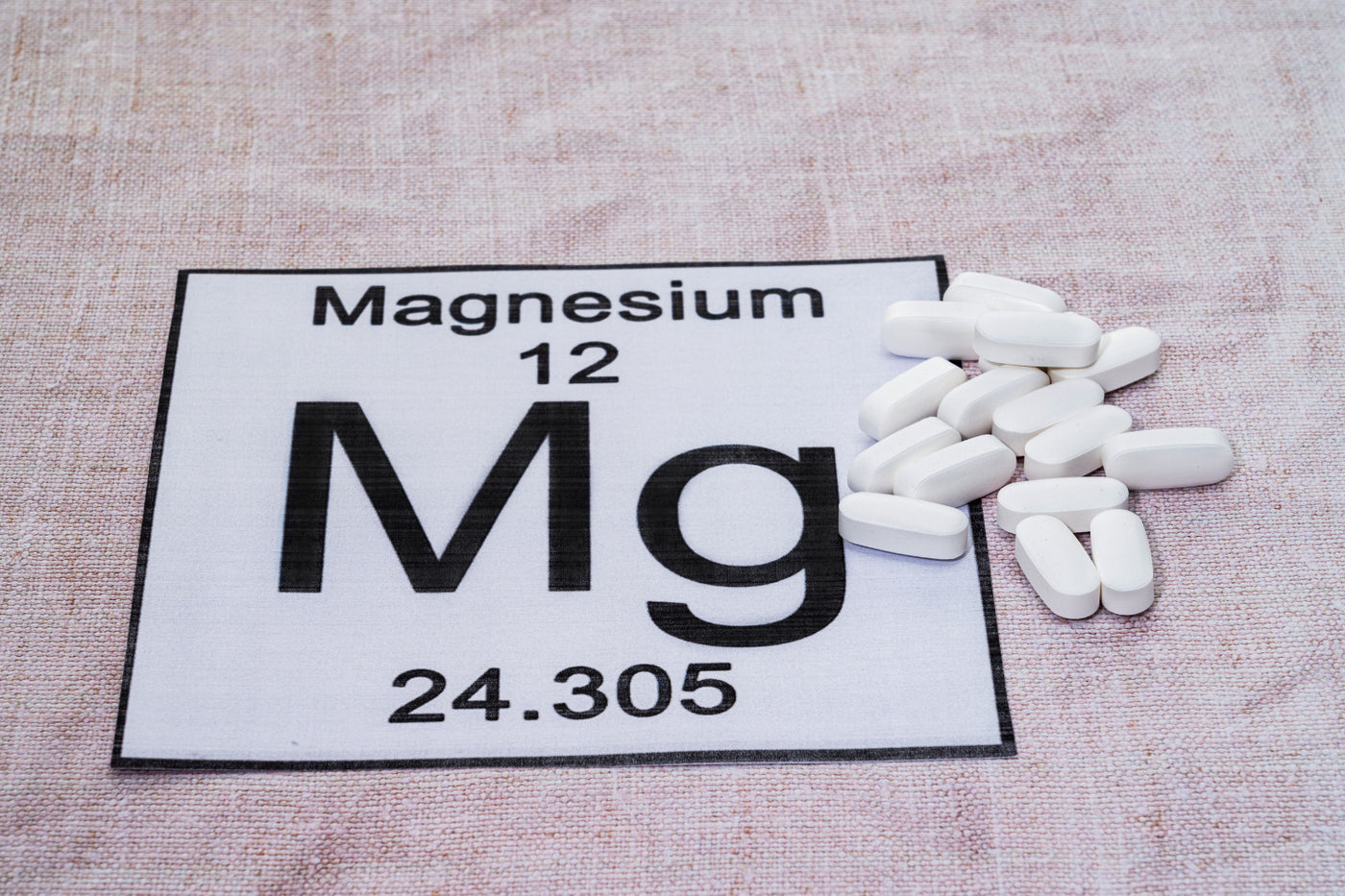 White magnesium tablets beside the Mg element symbol for an article about magnesium supplements for sleep