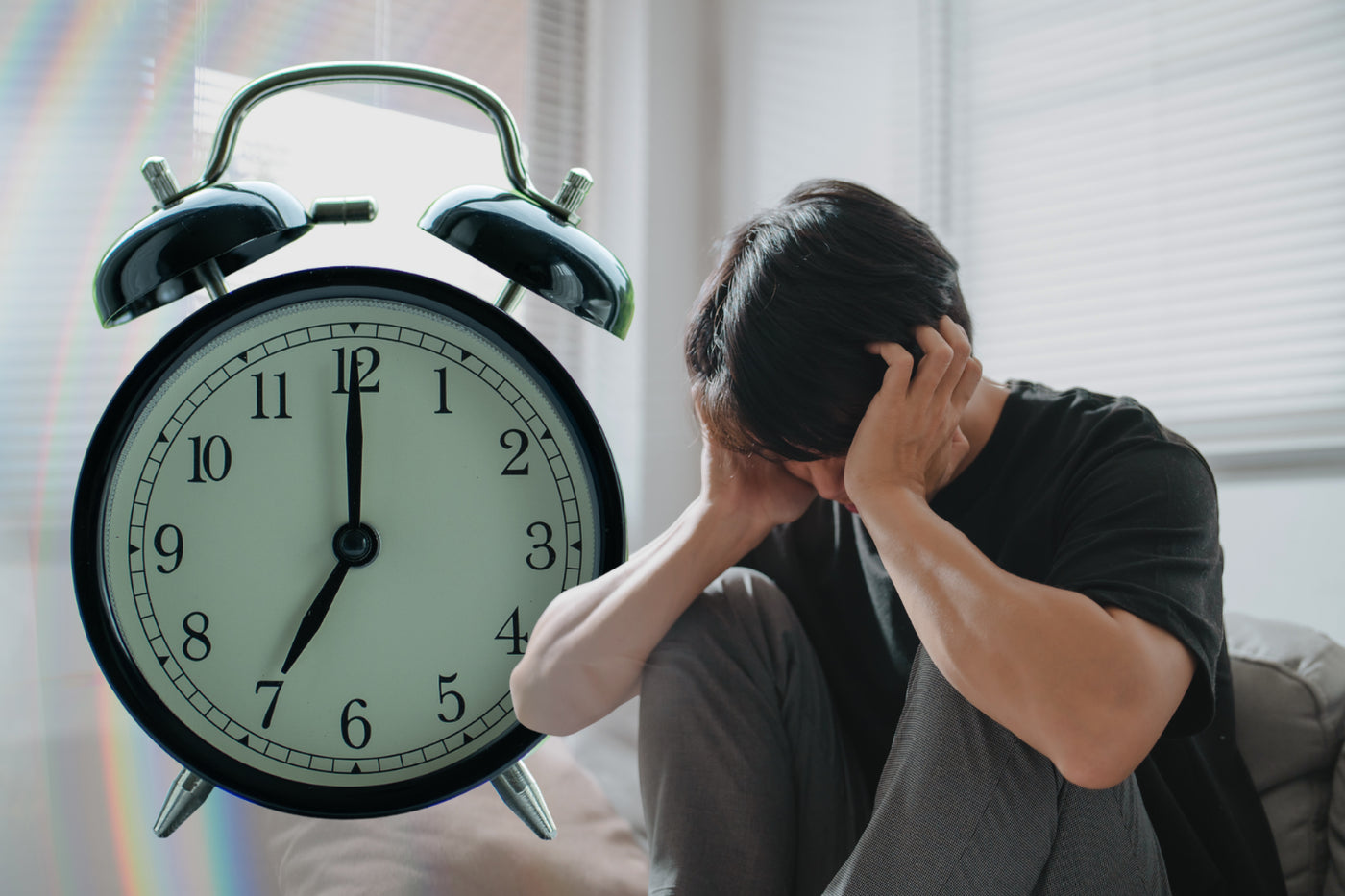 A stressed man sitting in bed holding his head in distress, superimposed with a large alarm clock showing seven o'clock.