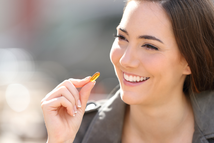 A person holds a yellow capsule between their fingers and smiles broadly.