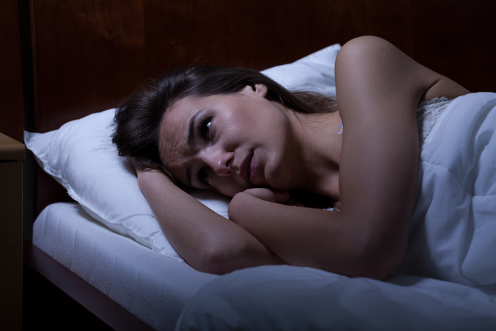 A person lying awake in bed with a worried expression.