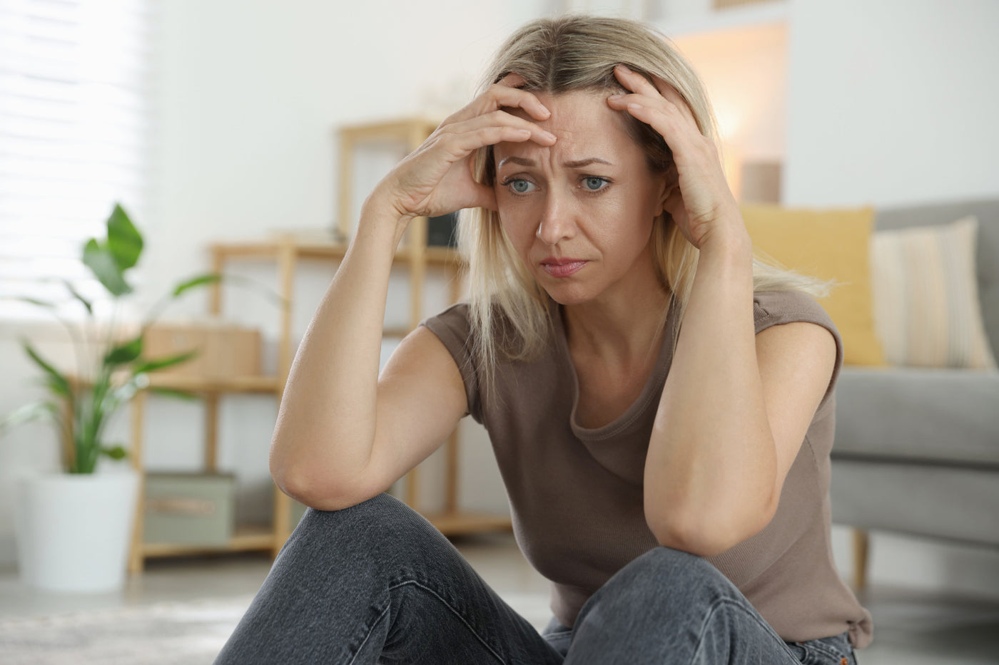Woman sitting with her hands on her head looking overwhelmed, representing emotional stress and anxiety linked to perimenopause hormone fluctuations.