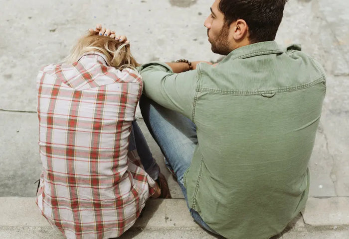 Couple sitting on a curb with woman holding hands and face in frustration.