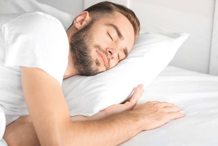 A person sleeping on a white pillow and bed with their eyes closed.