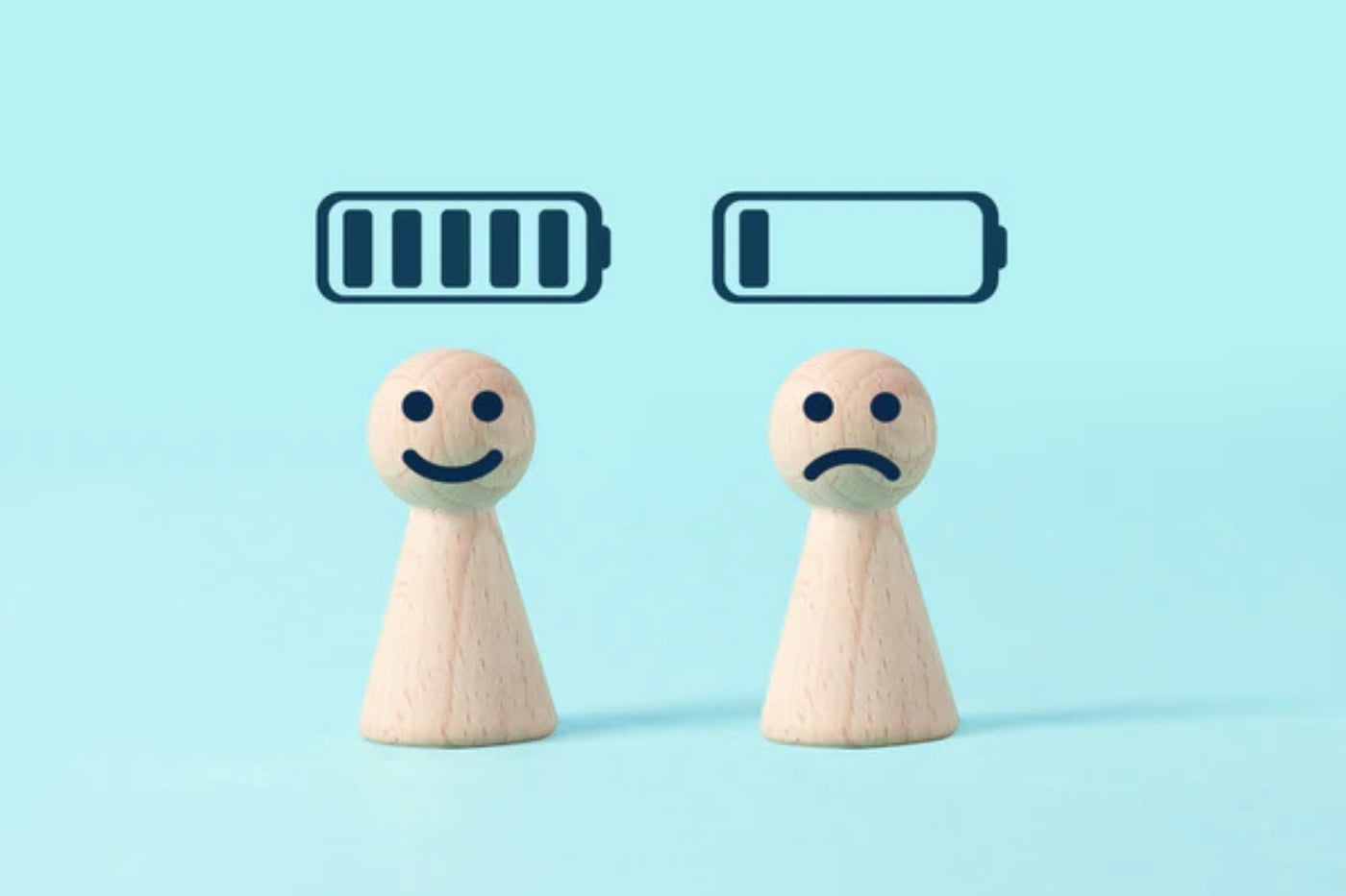 Two wooden peg figures with smiling and frowning faces beneath full and empty battery icons, illustrating the concept of a recharged versus drained social battery.