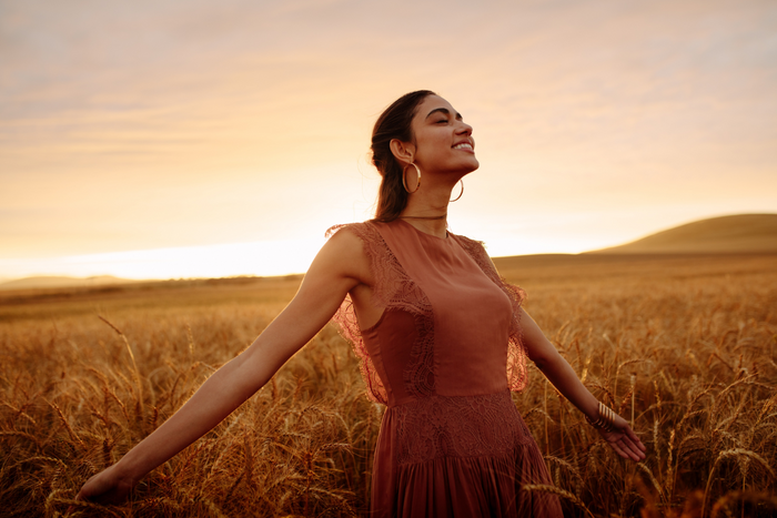 Woman looking happy in a field during sunset.