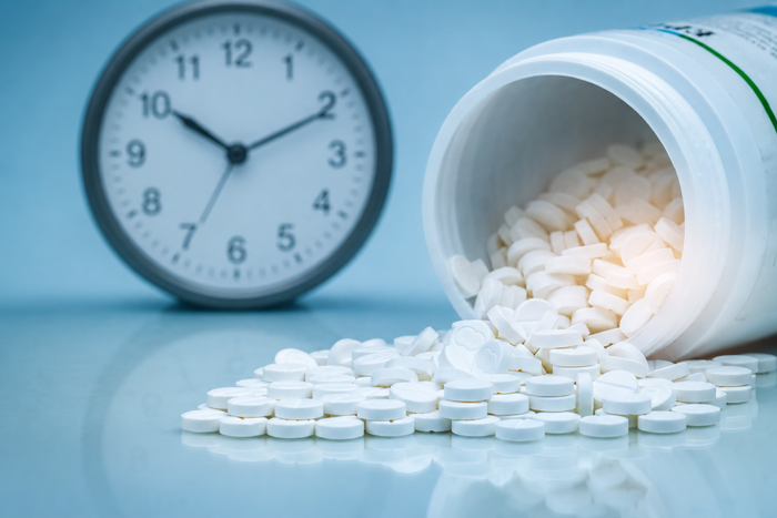 A close-up of scattered stress-relief supplements on a blue surface, with an open pill bottle spilling tablets beside a clock.