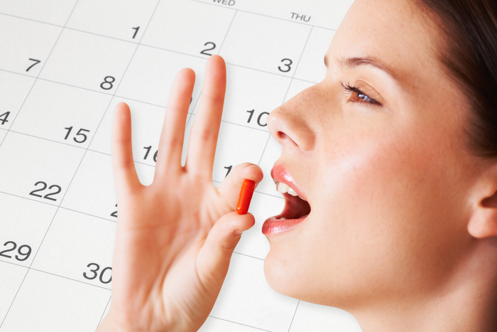 Woman taking a daily supplement capsule with a calendar in the background.