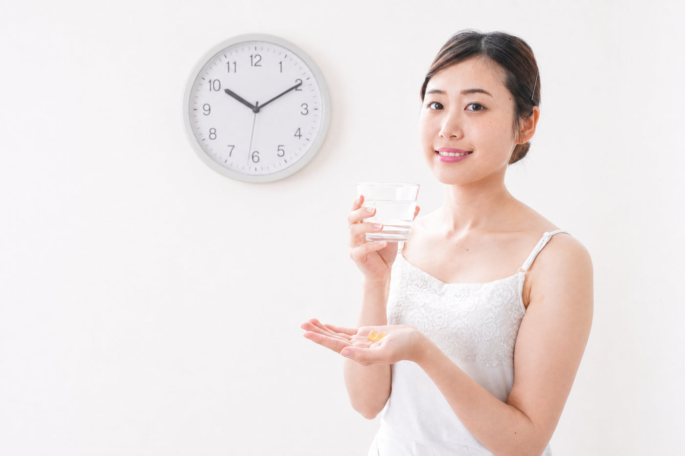 Woman holding magnesium supplements and a glass of water beside a clock, representing the best time to take magnesium in the morning or at night.