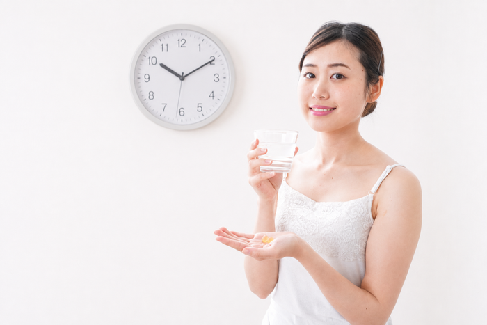 Woman holding magnesium supplements and a glass of water beside a clock, representing the best time to take magnesium in the morning or at night.