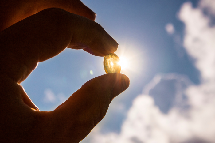 Hand holding a vitamin D capsule against sunlight
