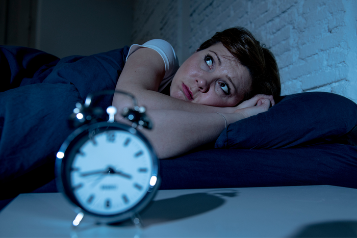 Woman lying awake in bed at night staring upward with an alarm clock in the foreground showing the late hour.