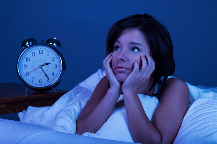 A woman lying awake in bed with a clock nearby, struggling with racing thoughts at night.