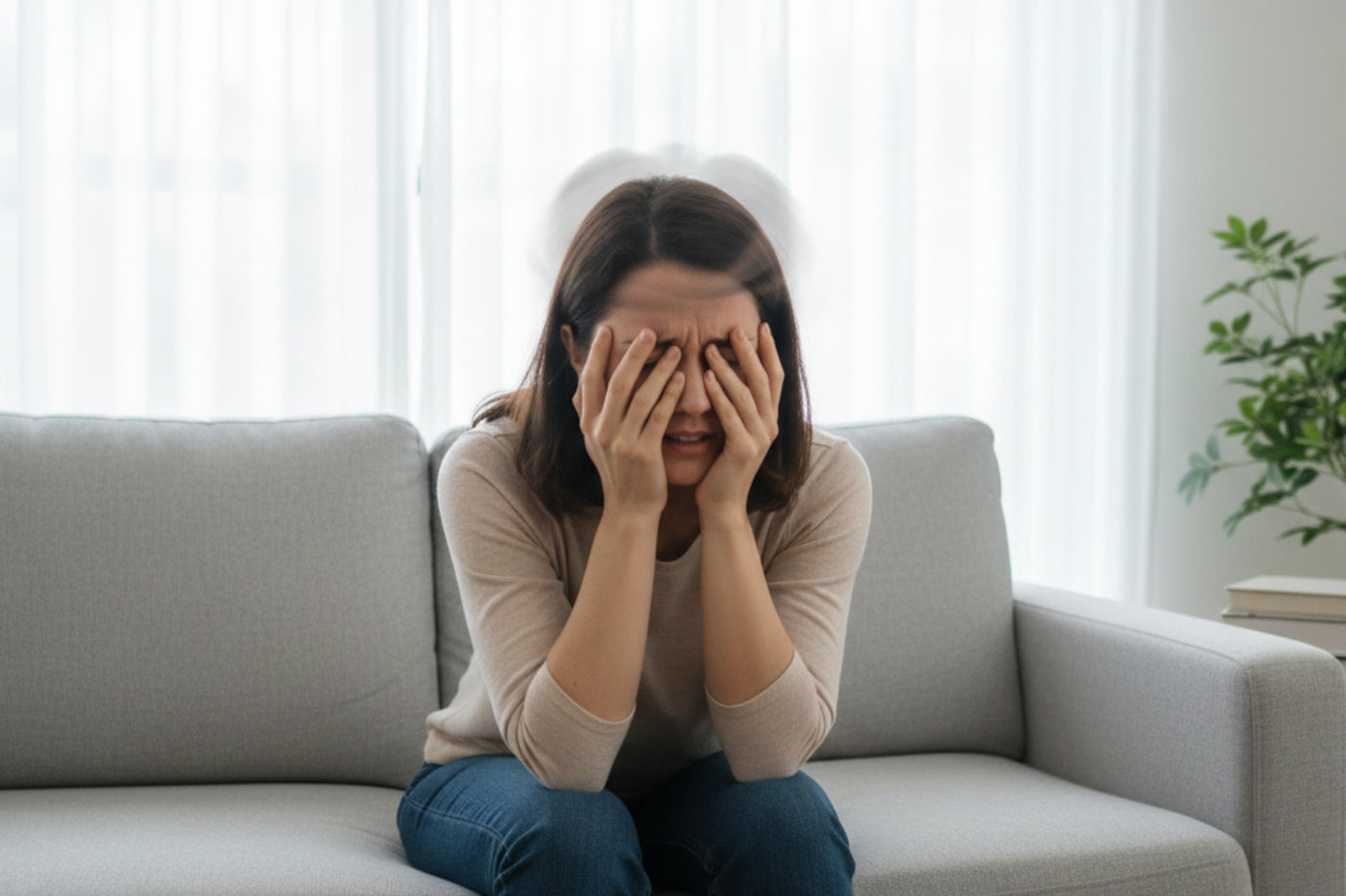 A person sitting on a couch covering their face with their hands.