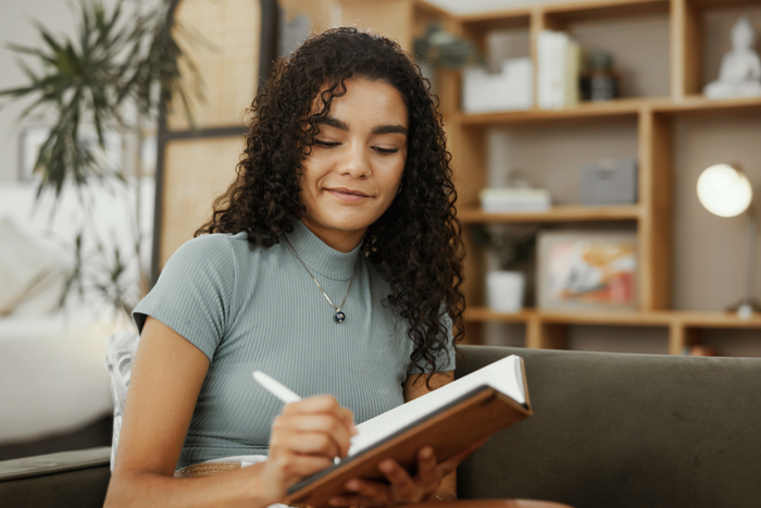Woman sitting on couch writing journal prompts for anxiety in notebook